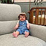 Olive is registered to the contest to win money with this photo: baby, child, smiling, hat, overalls, blue_clothing, knitted_hat, armchair, furniture, indoor, crib, plant, happy, cute, infant, person, portrait, sitting, home, cozy