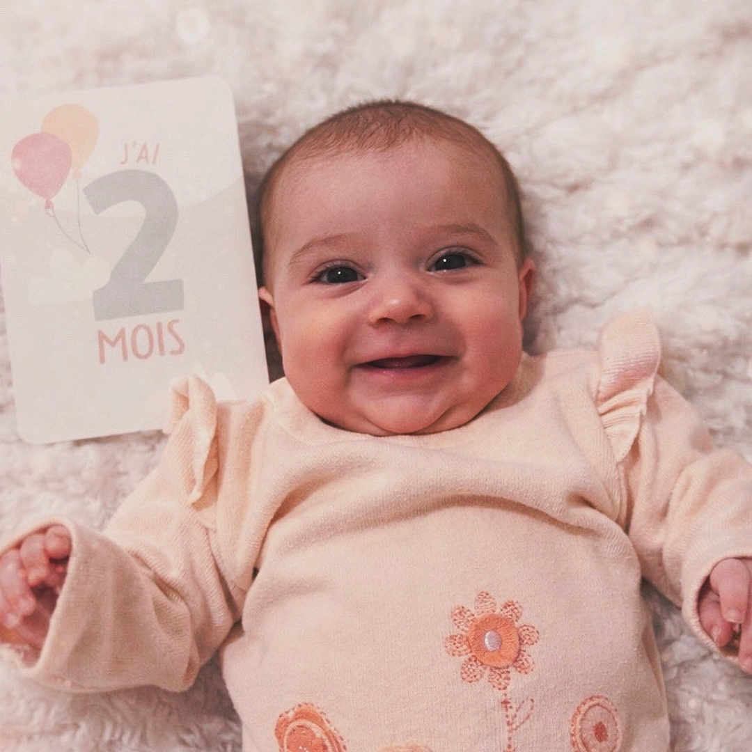 Joy a rejoint le concours — aidez-le/la à gagner de superbes lots ! baby, baby_girl, blanket, child, closeup, clothing, cozy, cute, face, floral_pattern, happy, indoors, infant, lying_down, milestone_card, newborn, portrait, smile, soft_toys, warm_colors