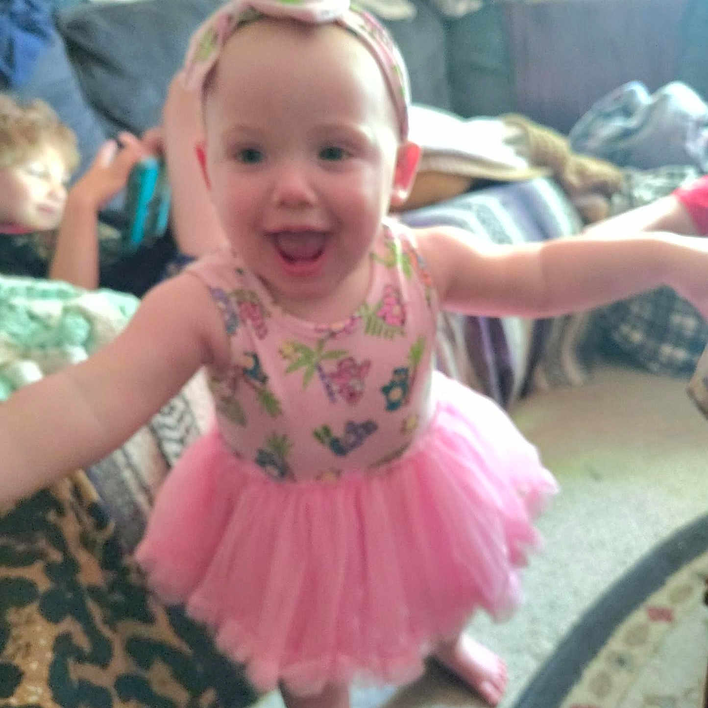 Briar joined the competition — help win amazing prizes! toddler, child, pink_tutu, headband, smiling, indoor, carpet, couch, person, happy, blurred_background, family, home, playful, barefoot, clothing, toy, living_room, blanket, leopard_print