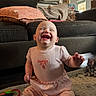 Briar is registered to the contest to win money with this photo: baby, laughing, pink_outfit, sitting, carpet, couch, cushion, indoor, child, happy, smiling, floor, toy, home, person, infant, cute, clothing, living_room, joy