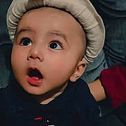 Wali Haider joined the competition — help win amazing prizes! baby, child, hat, feather, wide_eyes, curious, portrait, face, expression, mouth_open, dark_background, clothing, cute, infant, looking_up, indoor, adorable, young, person, headwear