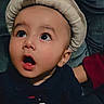 baby, child, hat, feather, wide_eyes, curious, portrait, face, expression, mouth_open, dark_background, clothing, cute, infant, looking_up, indoor, adorable, young, person, headwear