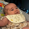 baby, infant, bib, clothing, face, smile, arm, child, indoor, seat, pattern, animal_print, bear, honeybee, person, cute, young, soft_lighting, closeup, happy