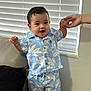 toddler, child, smiling, blue_clothing, floral_pattern, standing, couch, indoor, hand_holding, adult_hand, happy, cute, portrait, window_blinds, home, jewelry, shorts, shirt, person, young_child