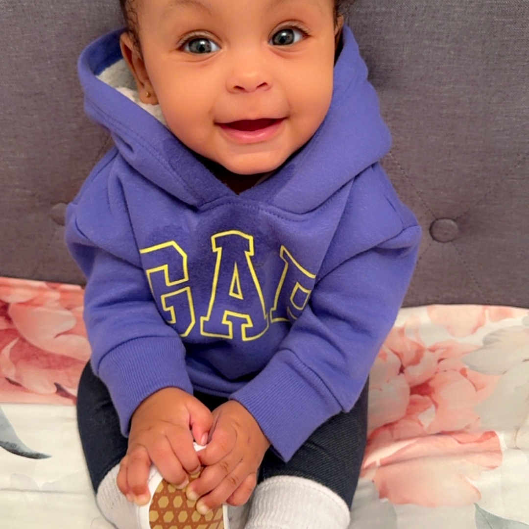 Leilani joined the competition — help win amazing prizes! baby, bodypart, clothing, coat, couch, face, finger, furniture, hand, head, hoodie, jacket, knitwear, pants, person, photography, portrait, sitting, sweater, sweatshirt