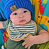 baby, infant, blue_hat, striped_bib, green_onesie, colorful_playmat, giraffe_design, cute, child, indoors, seated, toy, fabric, knit_hat, expression, face, hand, comfort, young, playtime