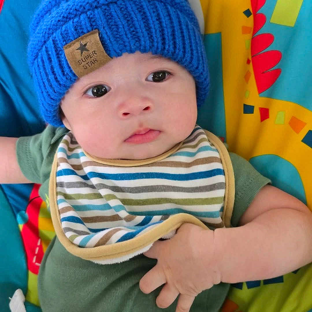 Clarence Axel is registered to the contest to win money with this photo: baby, blue_hat, child, colorful_playmat, comfort, cute, expression, fabric, face, giraffe_design, green_onesie, hand, indoors, infant, knit_hat, playtime, seated, striped_bib, toy, young