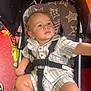 toddler, child, stroller, safety_harness, striped_clothing, toy, star_pattern, cushion, curious, indoor, casual, baby, seat, footwear, blue_socks, expression, portrait, infant, young_child, person