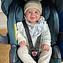 baby, child, car_seat, smile, hat, knit_hat, straps, clothing, indoor, seat, safety, cute, infant, person, portrait, happy, young_child, warm_clothes, wood_floor, cozy