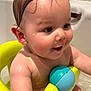 baby, bath, bathtub, child, water, toy, yellow_bath_seat, blue_ball, wet_hair, splashing, smiling, skin, arm, ear, face, bath_brush, tile_wall, infant, sitting, cute