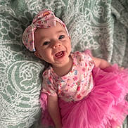 Harmony is registered to the contest to win money with this photo: baby, child, smiling, headband, pink_tutu, floral_pattern, happy, infant, clothing, blanket, portrait, cute, joyful, face, person, toddler, apparel, fabric, lying_down, indoor