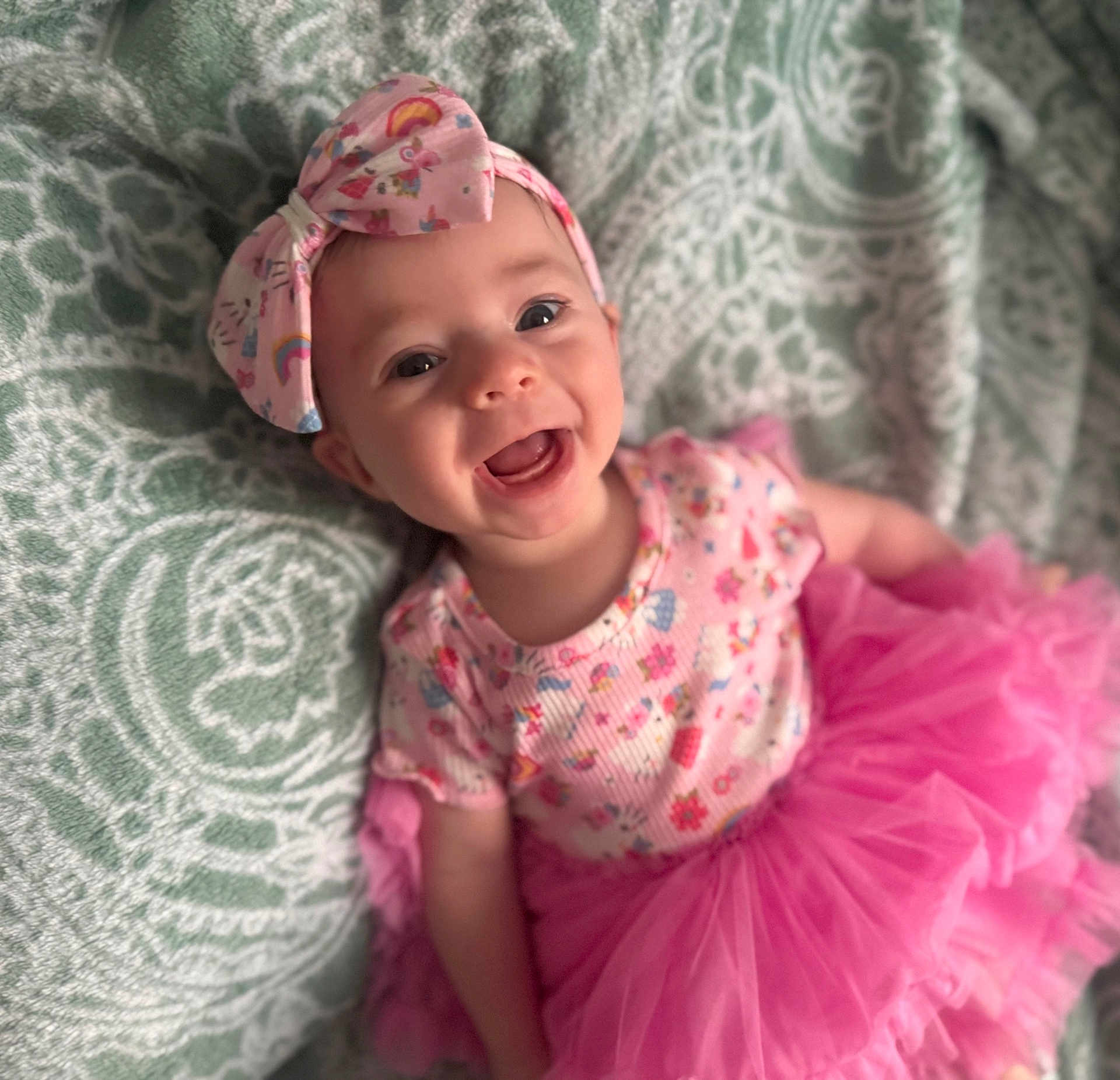 Harmony is registered to the contest to win money with this photo: baby, child, smiling, headband, pink_tutu, floral_pattern, happy, infant, clothing, blanket, portrait, cute, joyful, face, person, toddler, apparel, fabric, lying_down, indoor