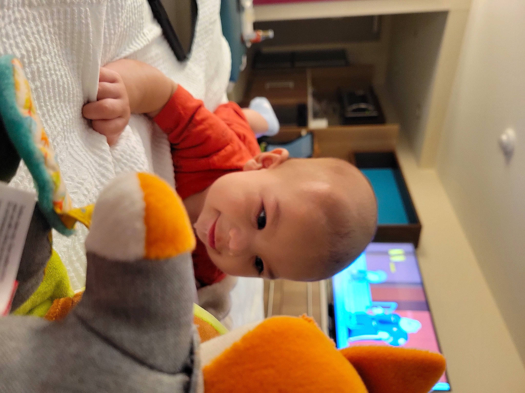 Darwin is registered to the contest to win money with this photo: baby, baby_products, baby_toys, child, comfort, finger, flooring, fun, happy, orange, person, play, plush, room, shelf, sitting, smile, stuffed_toy, toddler, toy