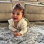 baby, child, crawling, smile, happy, indoor, rug, carpet, furniture, sofa, hair_clip, curly_hair, white_shirt, green_pants, cute, portrait, person, home, floor, bright