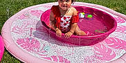 Viviana joined the competition — help win amazing prizes! toddler, child, pool, water, splash, pink, swimsuit, outdoor, grass, sunny, backyard, fence, trees, curly_hair, happy, summer, play, toy, water_toy, sitting
