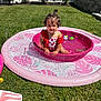 toddler, child, pool, water, splash, pink, swimsuit, outdoor, grass, sunny, backyard, fence, trees, curly_hair, happy, summer, play, toy, water_toy, sitting
