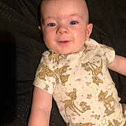 Colby is registered to the contest to win money with this photo: baby, child, infant, smiling, lying_down, onesie, deer_print, cute, happy, face, skin, short_sleeves, young_child, indoors, portrait, person, toddler, apparel, expression, sleepwear