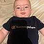 Colby joined the competition — help win amazing prizes! baby, child, infant, face, pout, blue_shirt, champion_logo, shadow, blanket, laying_down, curious_expression, short_hair, indoor, casual_clothing, tshirt, person, young, skin, head, portrait