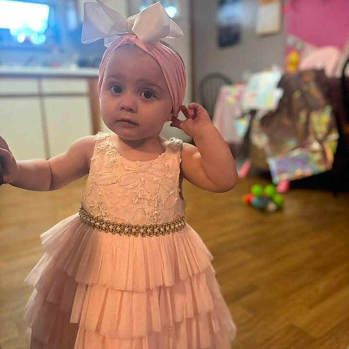 Jorniee is registered to the contest to win money with this photo: bow, child, clothing, curious_expression, cute, decor, floor, furniture, girl, headband, home, indoor, pink_dress, portrait, soft_lighting, standing, toddler, toy, wooden_floor, young_child