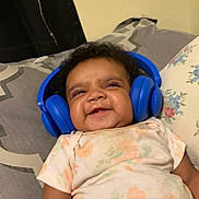 Willow joined the competition — help win amazing prizes! baby, headphones, smiling, bed, pillow, blanket, person, child, cute, happy, indoors, clothing, floral, relaxing, cozy, infant, face, expression, room, sleepwear