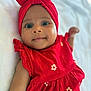 baby, infant, child, red_dress, headwrap, smile, face, eyes, arm, lying_down, soft_surface, cute, portrait, closeup, apparel, fabric, flower_pattern, skin, happy, indoors