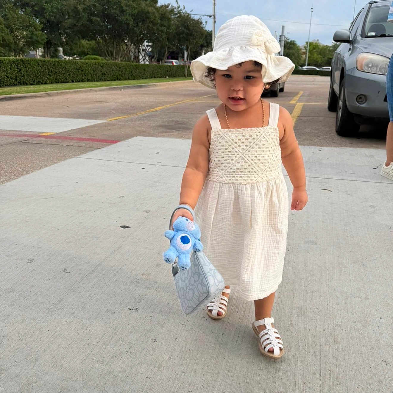 Sahily Arlet joined the competition — help win amazing prizes! accessory, car, child, cute, daytime, girl, outdoor, parking_lot, person, purse, sandals, sidewalk, stuffed_toy, summer, sunhat, toddler, toy, walking, white_dress, young_child