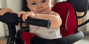 Maëlan participe au concours pour gagner de l'argent avec cette photo : baby, child, clothing, cute, expression, face, foot, handlebar, home, indoor, infant, light, person, playful, red, safety_bar, seat, smile, stroller, toddler
