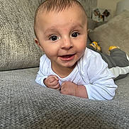 Khalil joined the competition — help win amazing prizes! baby, child, closeup, couch, cozy, cushion, expression, face, grey_pants, happy, home, indoor, infant, lying_down, person, portrait, skin, smiling, white_shirt, yellow_socks
