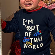 Malik joined the competition — help win amazing prizes! toddler, child, smiling, curly_hair, pajamas, space_theme, indoor, barefoot, clothing, carpet, doorway, wall, person, happy, young_child, cute, standing, home, room, playful