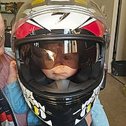 Nino participe au concours pour gagner de l'argent avec cette photo : child, helmet, motorcycle_helmet, face, reflection, indoor, person, adult_hand, clothing, jacket, blue_sleeve, room, door, floor, furniture, toy, casual, closeup, portrait, safety_gear