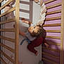 baby, child, crib, wooden_crib, plush_toy, elephant_toy, cushion, pastel_colors, purple_wall, curly_hair, looking_up, sleeping_area, indoor, bedroom, soft_lighting, infant_clothing, red_pants, blue_shirt, playtime, cute