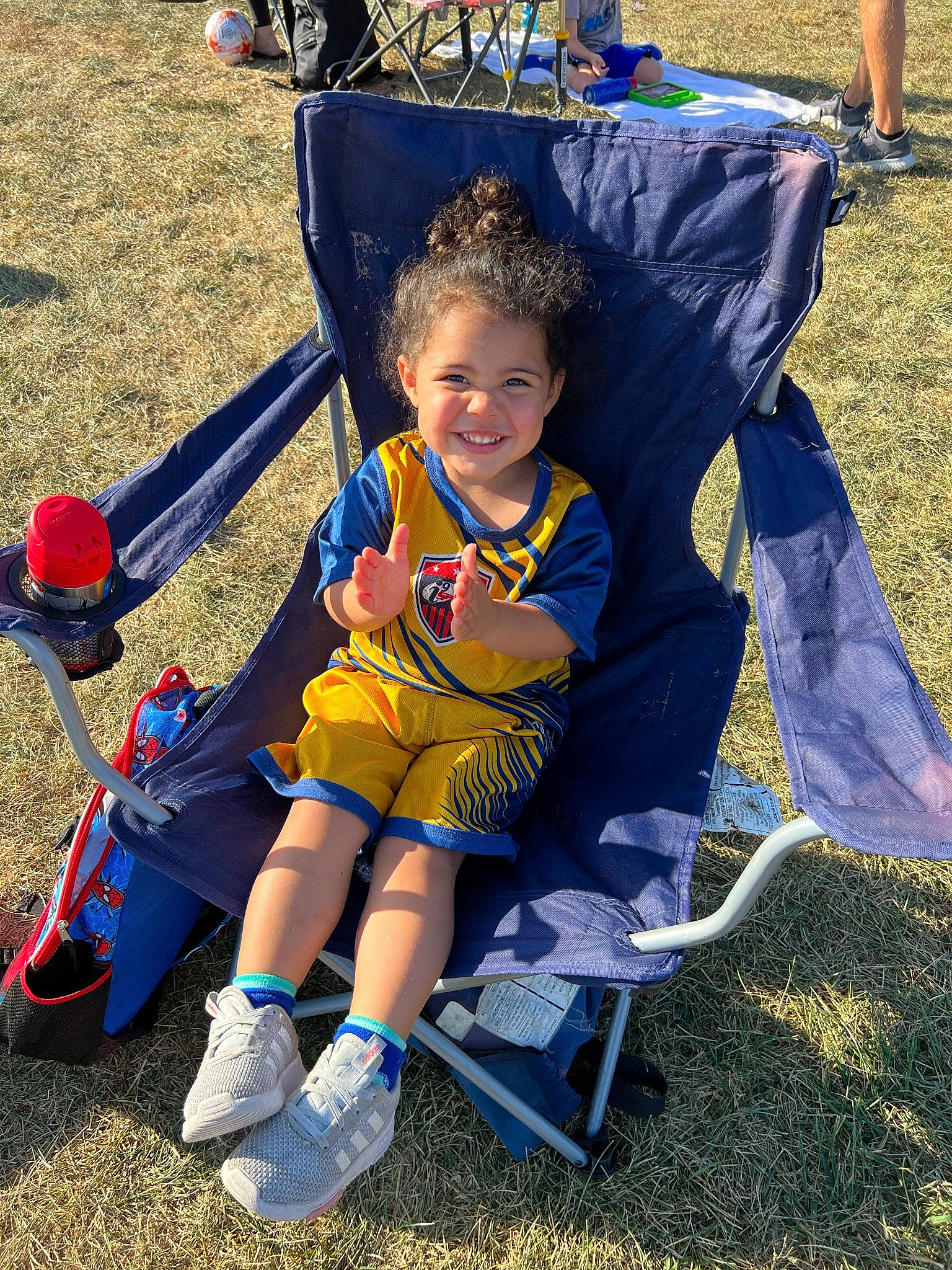 Kennedi is registered to the contest to win money with this photo: baby_products, chair, child, electric_blue, event, folding_chair, fun, grass, happy, joy, leisure, outdoor_play_equipment, person, personal_protective_equipment, play, recreation, shorts, sitting, smile, toddler