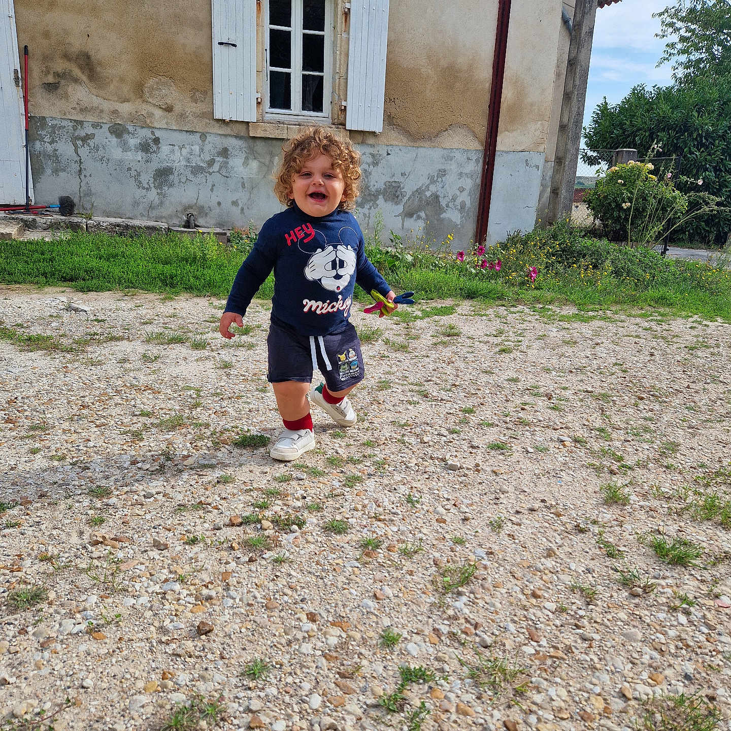 Lucyan a rejoint le concours — aidez-le/la à gagner de superbes lots ! child, clothing, curly_hair, daylight, flowers, grass, gravel, happy, house, outdoor, person, running, shorts, shutters, sky, smile, sweater, toddler, toy, window