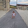 toddler, child, pacifier, curly_hair, road, rural, stone_building, sunset, sky, barefoot, walking, outdoor, nature, vintage, countryside, pathway, person, small_child, alone, exploration