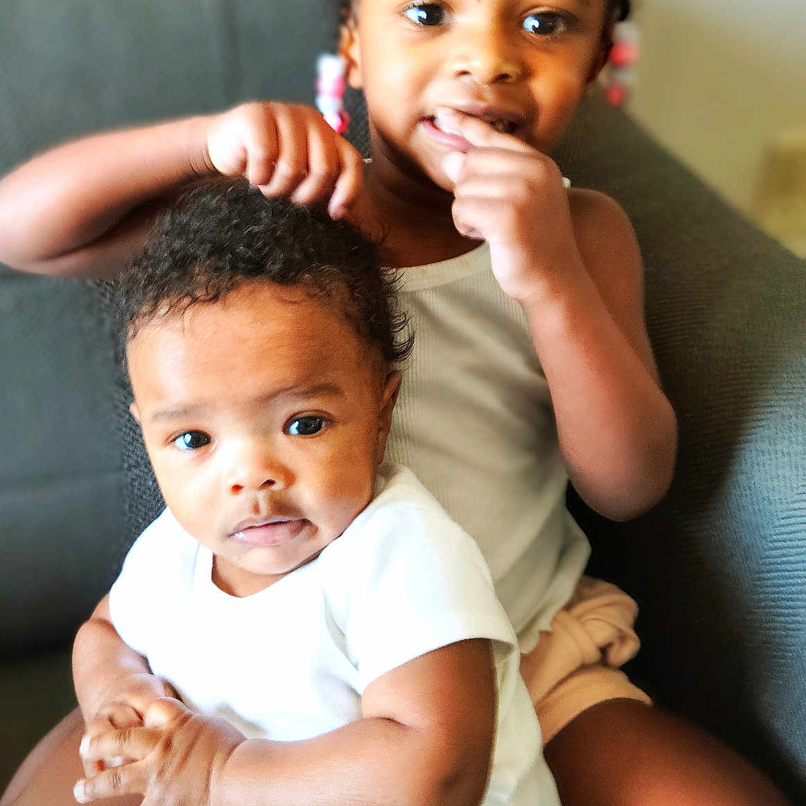 Jeremiah Folks is registered to the contest to win money with this photo: baby, black_hair, casual, child, couch, curly_hair, cute, family, home, indoor, interaction, person, playful, portrait, seated, sibling, smiling, toddler, white_clothing, young_child