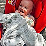 baby, infant, car_seat, blanket, red, smiling, happy, outdoor, sunlight, cute, child, clothing, fabric, hand, face, person, seat, sitting, comfort, blanket_pattern