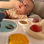 baby, drool, toy, activity_center, curious, child, indoor, soft_focus, face, expression, seat, clothing, person, play, colorful, infant, closeup, head, young, looking_up