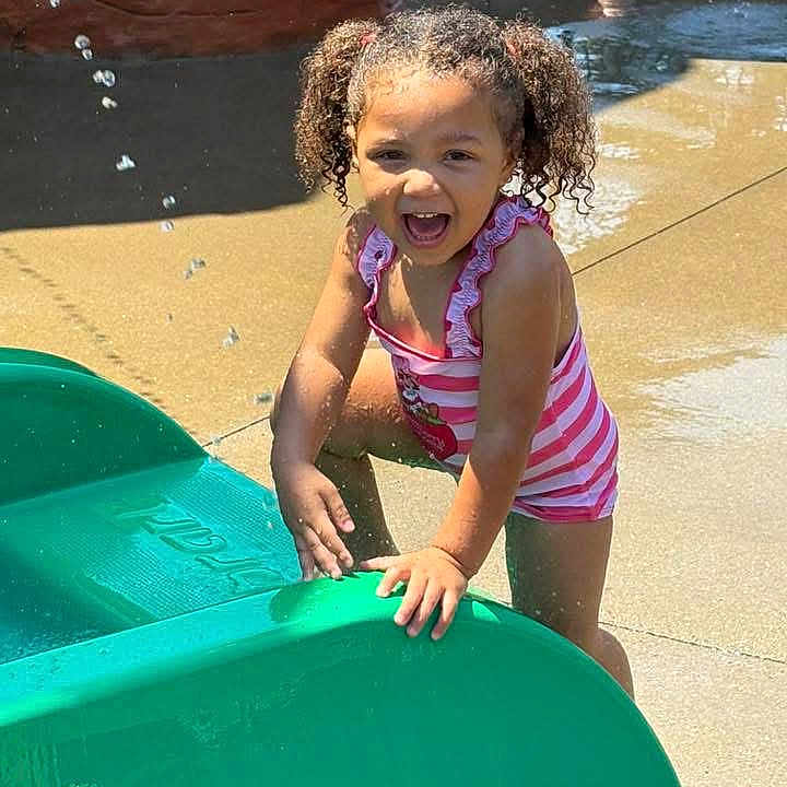 Tanylah is registered to the contest to win money with this photo: child, girl, water, playground, summer, smiling, curly_hair, pigtails, splash, outdoor, sunny, tankini, pink_stripes, fun, happy, slide, concrete, water_play, daylight, joy