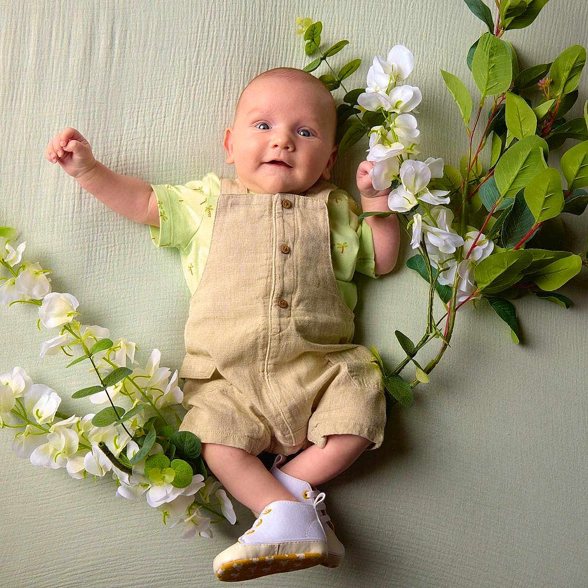 Jules participe au concours pour gagner de l'argent avec cette photo : baby, blanket, casual_clothing, child, cute, face, green_leaves, happy, indoors, infant, lying_down, nature, overalls, plant, portrait, small_hands, smiling, soft_light, white_flowers, white_shoes