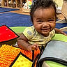 Rosalinda is registered to the contest to win money with this photo: baby, carpet, child, colorful, crawling, curly_hair, floor, green, happy, indoor, infant, orange, person, play_mat, red, room, smiling, toy, wooden_furniture, yellow