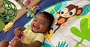 Rosalinda is registered to the contest to win money with this photo: baby, blue_carpet, cartoon, child, colorful, cushion, cute, fabric, face, floor, hand, happy, indoor, infant, monkey, person, play_mat, smiling, sock, toy