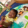 baby, blue_carpet, cartoon, child, colorful, cushion, cute, fabric, face, floor, hand, happy, indoor, infant, monkey, person, play_mat, smiling, sock, toy