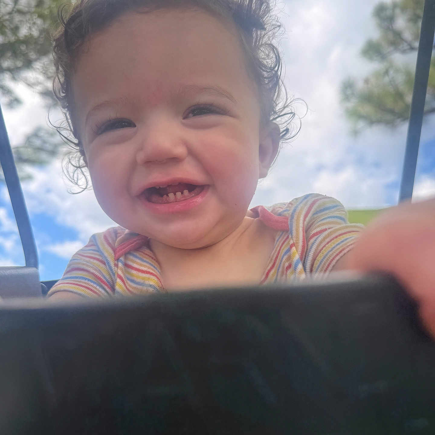 Leonardo is registered to the contest to win money with this photo: baby, child, closeup, clouds, colorful_clothing, curly_hair, cute, daylight, happy, holding_camera, joyful, nature, outdoor, person, playful, portrait, sky, smiling, toddler, trees
