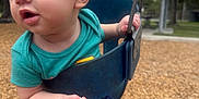 Leonardo is registered to the contest to win money with this photo: toddler, child, swing, playground, outdoor, wood_chips, green_shirt, blue_socks, curly_hair, park, daylight, metal, seat, hand, legs, nature, trees, fun, activity, young