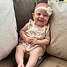 Amelia is registered to the contest to win money with this photo: baby, child, infant, smile, headband, flower, romper, sun_print, cushion, beige, wooden_bench, sitting, happy, cute, portrait, indoors, skin, feet, hands, person