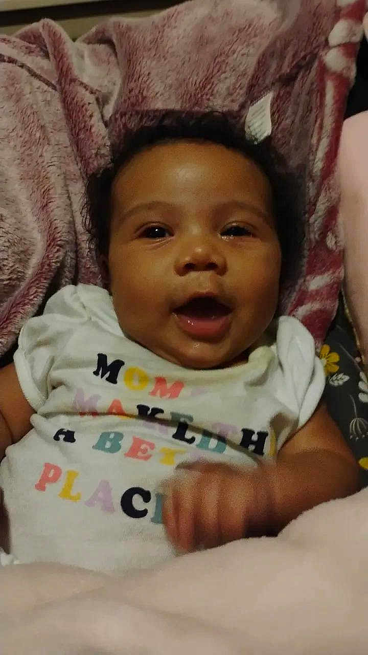 Gla'Zayah is registered to the contest to win money with this photo: baby, child, smiling, happy, infant, blanket, clothing, face, person, portrait, cute, young, soft_texture, indoors, lying_down, joyful, skin, hand, expression, toddler