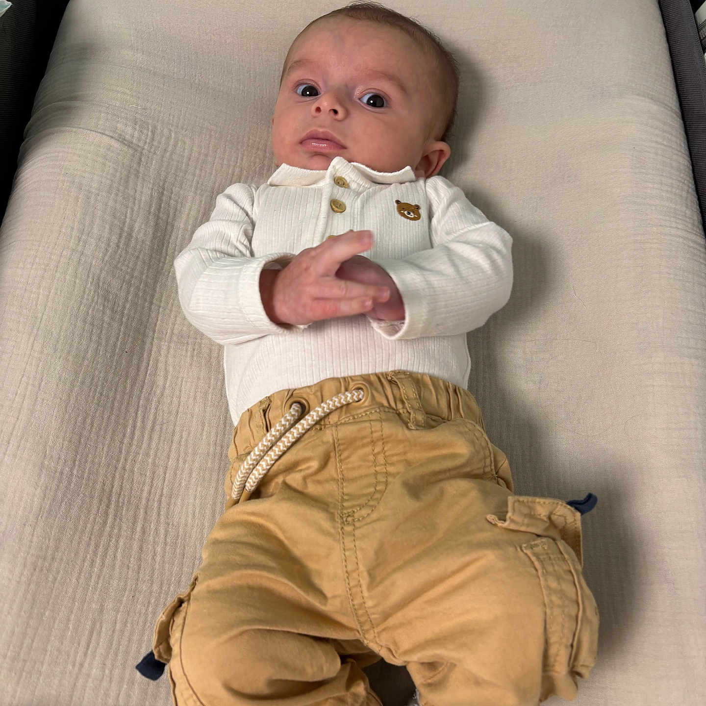 Télio a rejoint le concours — aidez-le/la à gagner de superbes lots ! baby, baby_garments, bedroom, changing_pad, child, clothing, cute, fabric, hands_together, indoor, infant, person, portrait, small_baby, socks, soft_lighting, tan_pants, white_top, wide_eyes, young_child