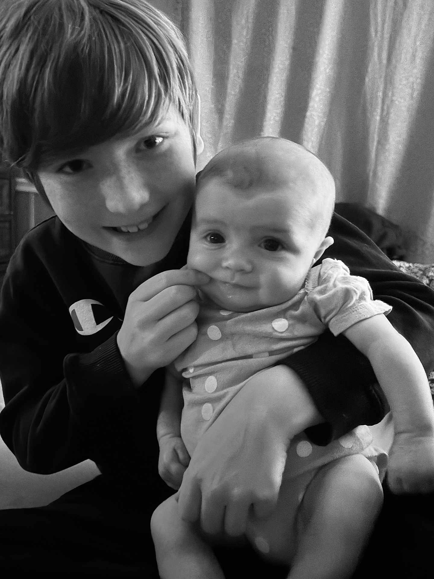 Aliki is registered to the contest to win money with this photo: black_and_white, child, baby, smiling, indoor, curtain, portrait, holding, playful, happy, face, person, cute, toddler, sibling, family, clothing, hand, expression, cozy