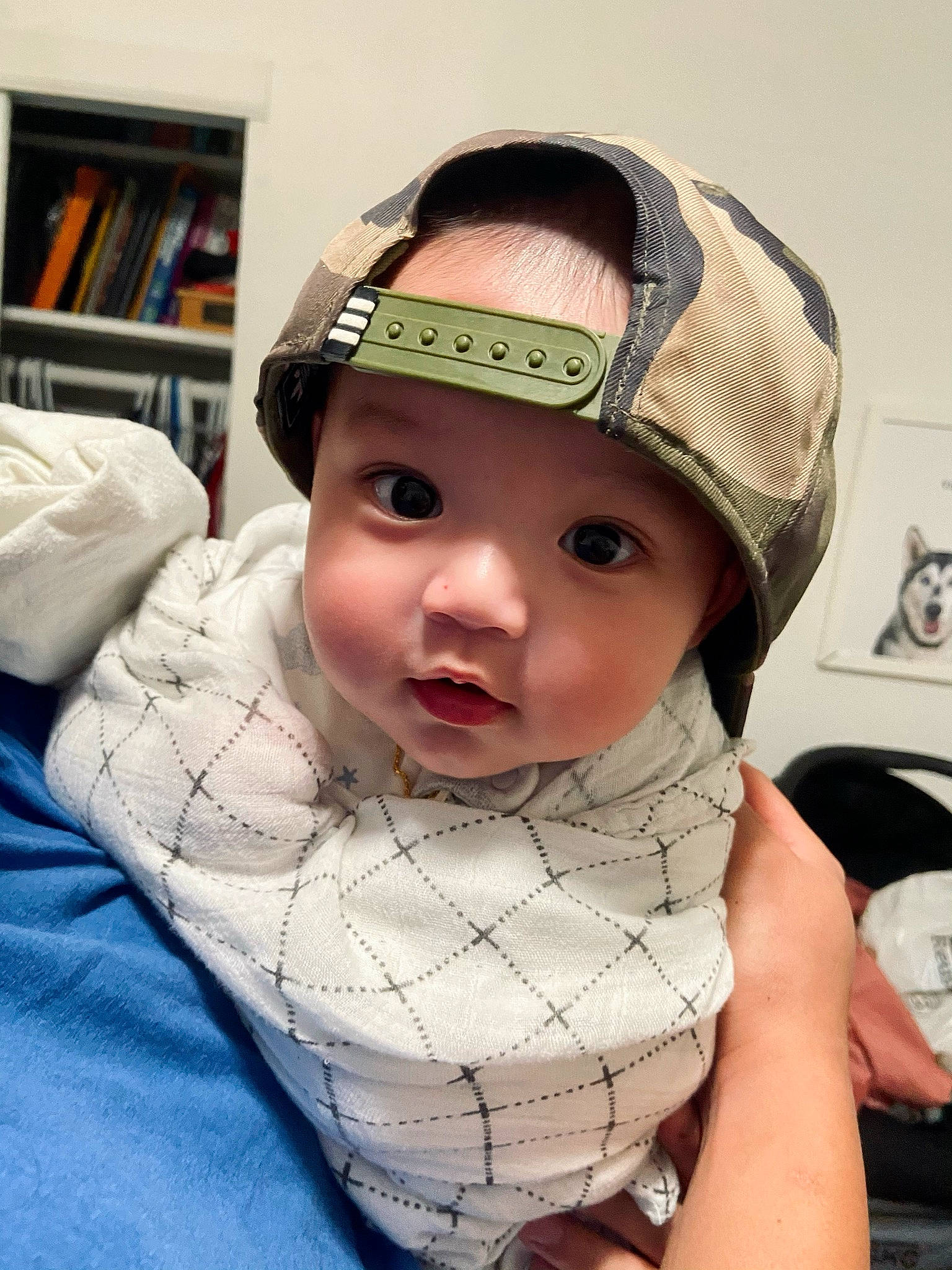 Rowan is registered to the contest to win money with this photo: baby, baby_toddler_clothing, bookcase, cap, cheek, chin, comfort, cool, eye, eyebrow, eyelash, fashion_accessory, headgear, headwear, lip, neck, pattern, person, personal_protective_equipment, shelf