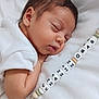 baby, sleeping, pacifier_clip, white_clothing, infant, closeup, face, skin, peaceful, rest, soft_lighting, cute, child, newborn, hand, fabric, portrait, indoors, calm, personalized